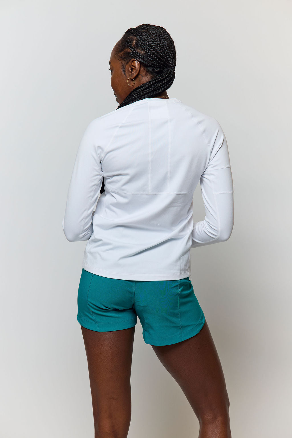 Model wearing Excel Sculpt Performance Shorts with a white long-sleeve top, showcasing active apparel from the back.