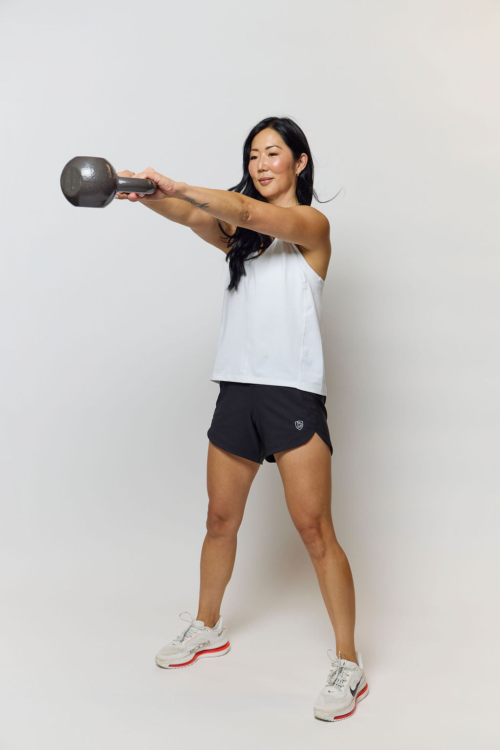 A woman wearing Excel Sculpt Performance Shorts exercising with a kettlebell, showcasing confidence and style.