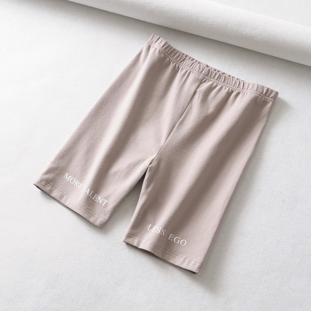 AlphaFlex performance training shorts in a soft beige color with 'MORE TALENT' and 'LESS EGO' text.
