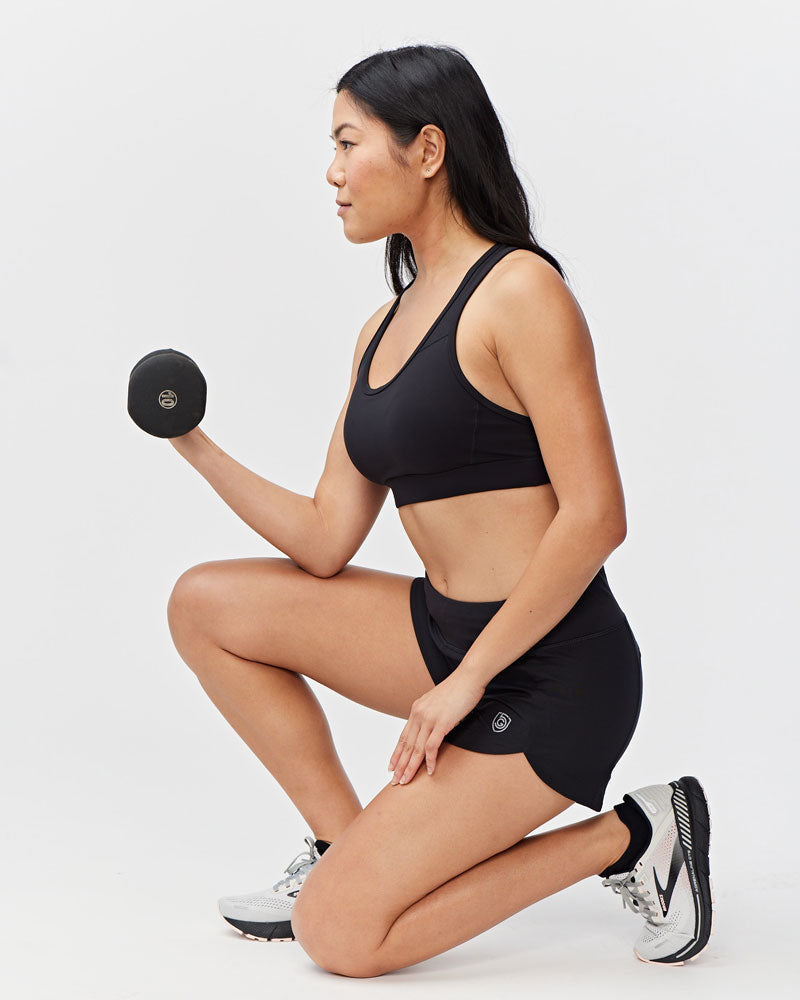 Woman in Excel Sculpt performance shorts exercising with dumbbell in a confident pose.