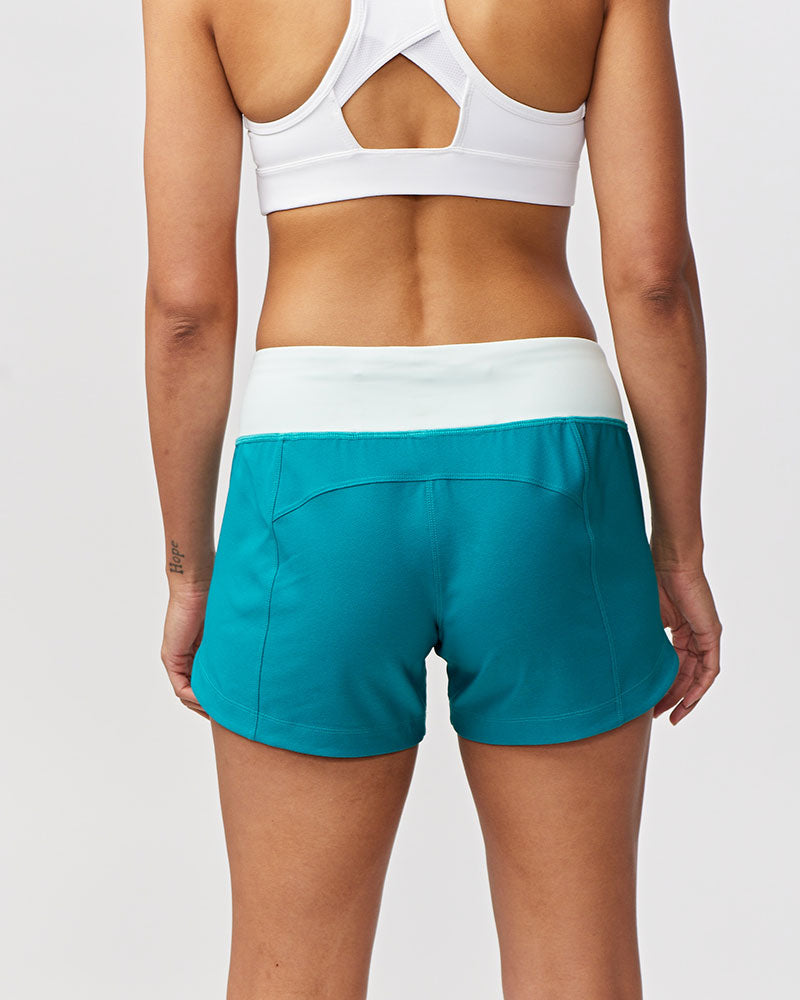 Back view of a woman wearing Excel Sculpt Performance Shorts in turquoise color with a white waistband.