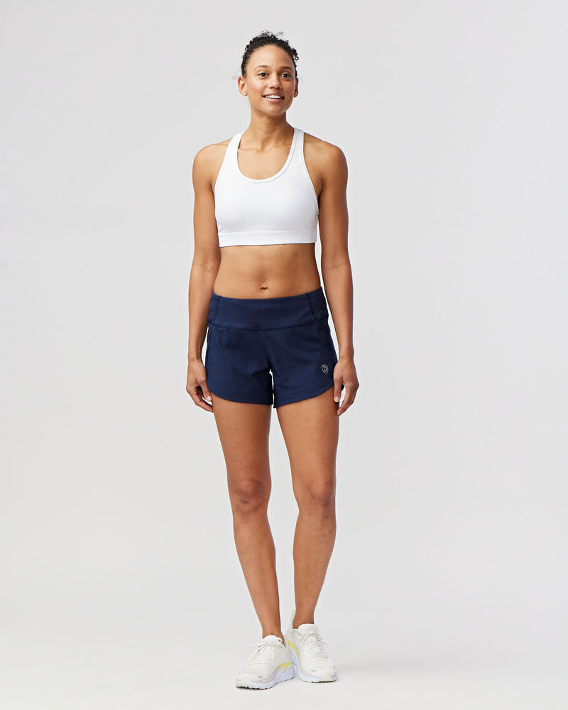 Woman standing in Excel Sculpt Performance Shorts and a sports bra, showcasing comfort and confidence in activewear.